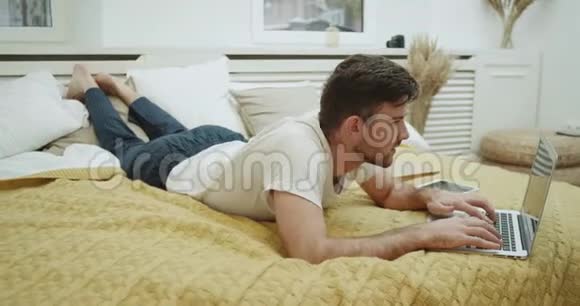 在一个现代的卧室里男人在床上工作在他的笔记本上非常集中视频的预览图