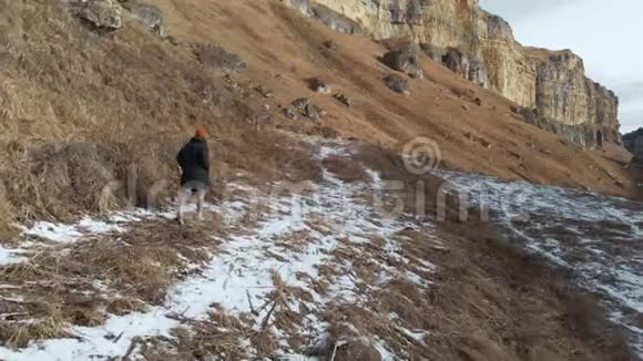 穿着羽绒服和帽子的女游客在岩石峡谷的初冬沿着小径散步黄色的草和碎片视频的预览图