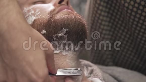 在理发店把剃须刀贴在时髦的胡子上刮胡子的人视频的预览图