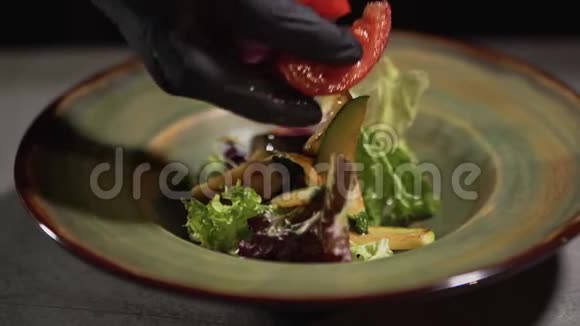 双手戴黑色食品手套将切碎的西红柿放在盘子上放在桌面上隔离在黑色背景上食物视频的预览图