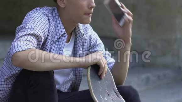 青少年男孩在智能手机上打电话给朋友骑滑板爱好视频的预览图