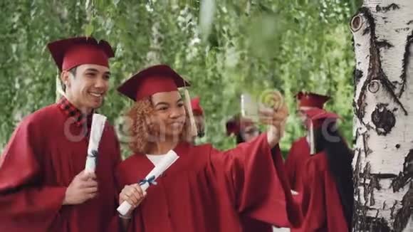 快乐的年轻人女孩和男孩在毕业典礼后自拍他们穿着长袍和文凭视频的预览图