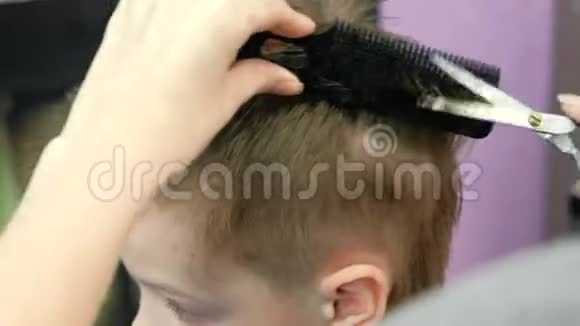理发师用剪刀梳理和剪金发短男孩的头发侧视视频的预览图