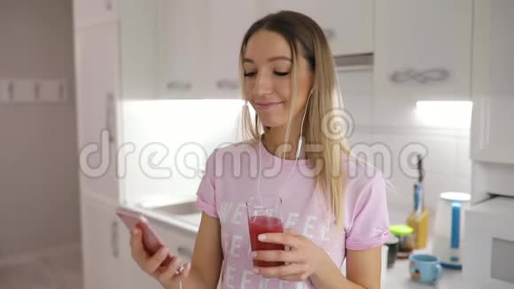 早上好女人在厨房喝果汁在家听音乐视频的预览图