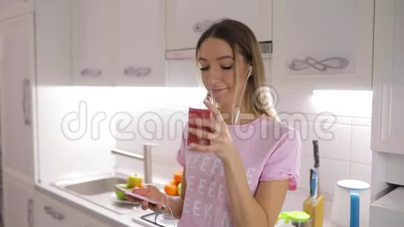 早上好女人在厨房喝果汁在家听音乐视频的预览图