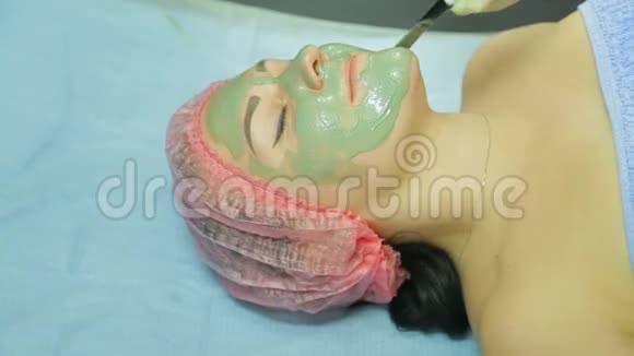 美容师在一个女人的脸上涂上一层灰色粘土的化妆面具视频的预览图