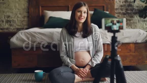 美丽的孕妇著名博主正在为关注智能手机摄像头和坐着聊天的人录制视频视频的预览图