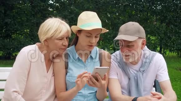 老人和女儿坐在公园里用手机浏览家庭在网上寻找方向视频的预览图