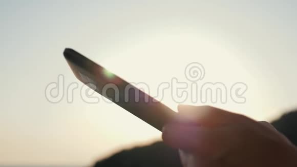 在日落时分一个女孩用平板电脑在太阳下的大海背景下工作视频的预览图