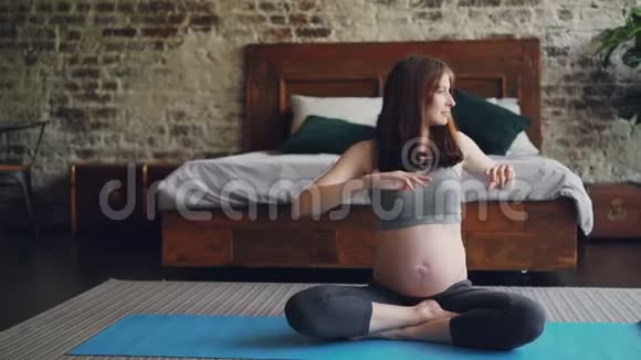 运动女准妈妈正在家里做运动坐在瑜伽垫上左右转动身体享受着快乐视频的预览图