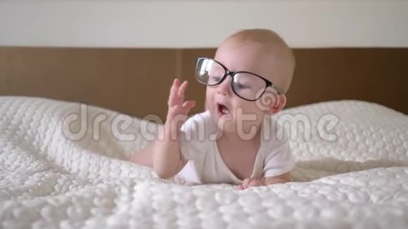婴儿时代戴着眼镜的蓝色大眼睛的可爱小男孩的画像躺在床上紧紧地视频的预览图