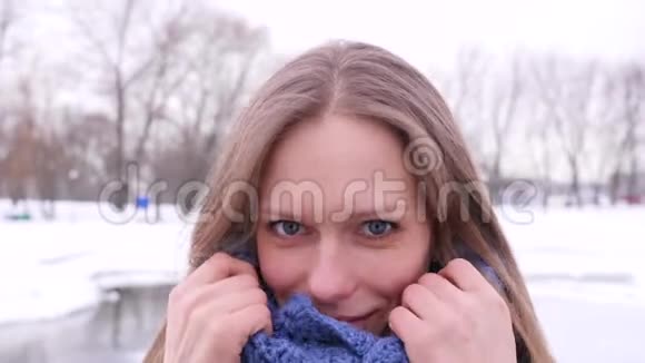 美丽的蓝眼女人在冬天的城市公园里她看着相机纠正她温暖的蓝色针织围巾视频的预览图