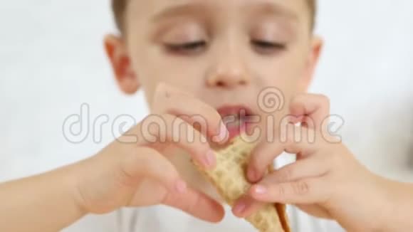 一个孩子很高兴在一个华夫饼锥里吃一个巧克力冰淇淋坐在桌子上背景是白色的重点视频的预览图