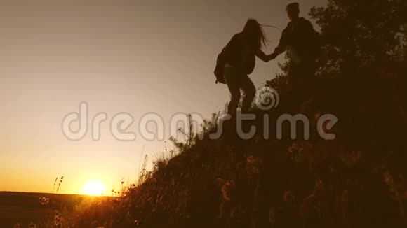 男性旅行者向攀登山顶的女性旅行者伸出手游客们在日落时分爬山手牵手视频的预览图