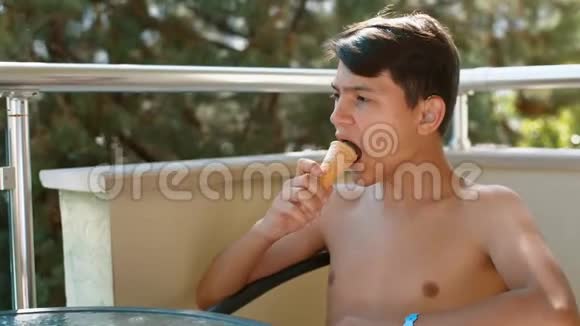 一个身材赤裸的年轻人坐在阳台上的玻璃桌前吃冰淇淋视频的预览图