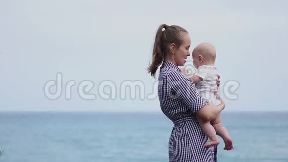 家庭幸福年轻的母亲在天空中抛起婴儿在晴天海滩上的肖像妈妈和小儿子积极正面视频的预览图