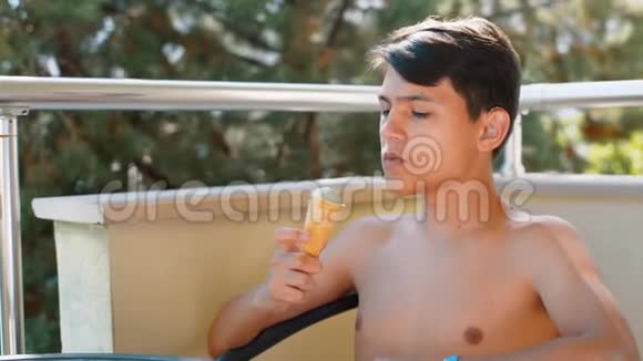 一个身材赤裸的年轻人坐在阳台上的玻璃桌前吃冰淇淋视频的预览图