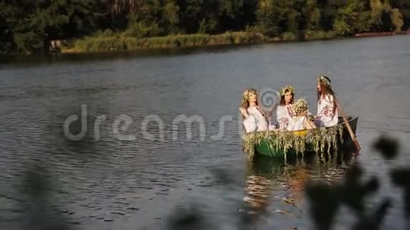 三个漂亮的女孩穿着斯拉夫的衣服坐在河上的一艘船上女人互相传递一束野花女孩视频的预览图