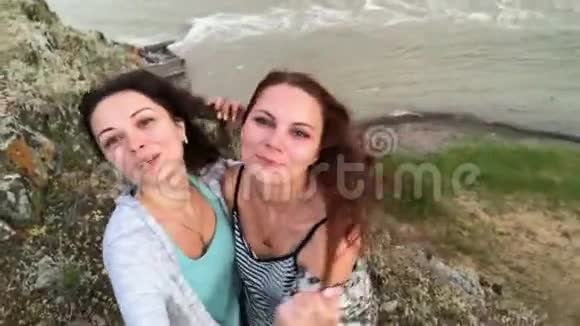 两个美丽的无忧无虑的女孩用智能手机自拍女人做滑稽的脸正面模特摆成粉红色视频的预览图