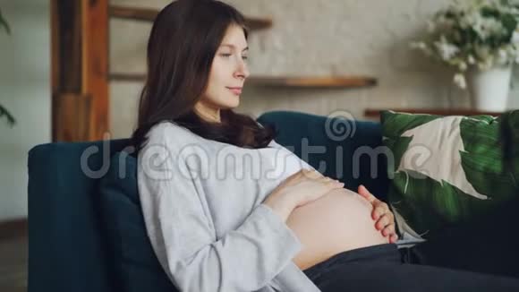 美丽的年轻女子期待母亲正在抚摸她的腹部看着它表达对未出生孩子的爱青年视频的预览图