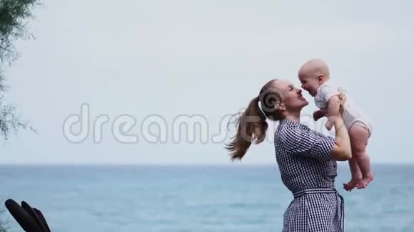 家庭幸福年轻的母亲在天空中抛起婴儿在晴天海滩上的肖像妈妈和小儿子积极正面视频的预览图