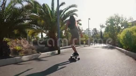 一个穿着短短裤的女孩在沙滩和棕榈树的道路上骑行视频的预览图