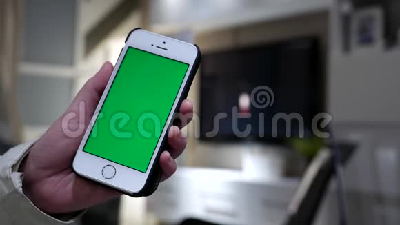 女人拿着绿色屏幕iphone和模糊的客厅视频的预览图