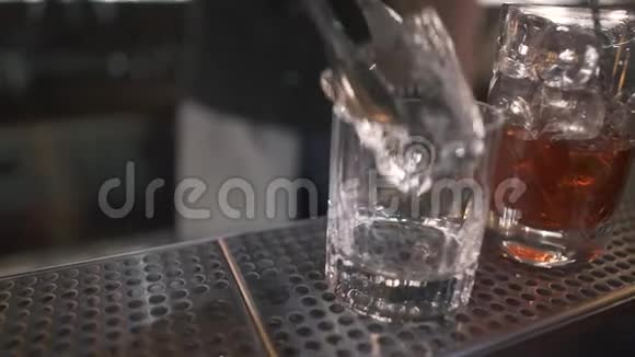 站在酒吧柜台上的小玻璃关闭酒保在柜台上用钳子把大冰块放进玻璃里视频的预览图
