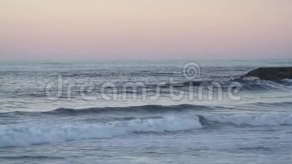 在雾蒙蒙的日落中海浪涌向沙滩视频的预览图