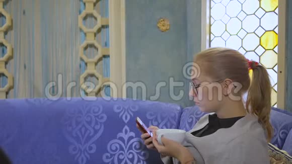戴眼镜的年轻女子坐在亚洲咖啡馆喝茶在智能手机上使用互联网视频的预览图
