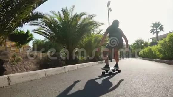 夏天在岛上女孩穿着短短裤在海滩和棕榈树附近的道路上长板骑行视频的预览图