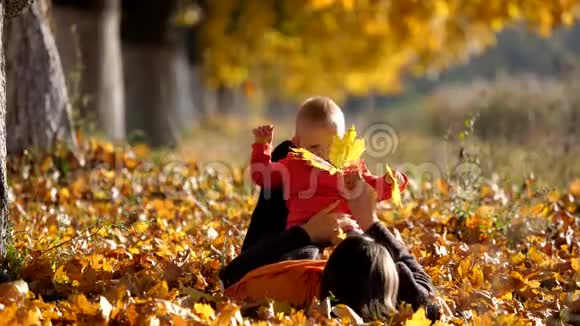 母亲仰卧在秋叶上和微笑的孩子玩耍视频的预览图