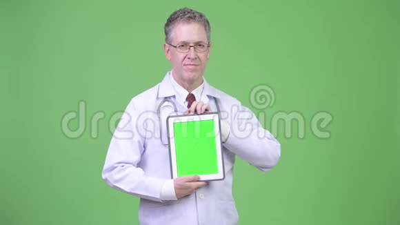 幸福成熟的男医生一边思考一边展示数码平板电脑的画像视频的预览图