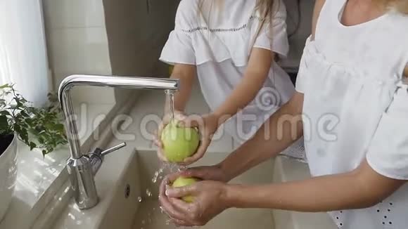 年轻漂亮的妈妈和她可爱的两个女儿一起洗厨房水槽里的绿苹果准备好准备视频的预览图