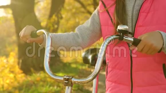 女孩的手拿着弯曲的自行车把手特写镜头女孩在秋天骑自行车在公园里散步视频的预览图