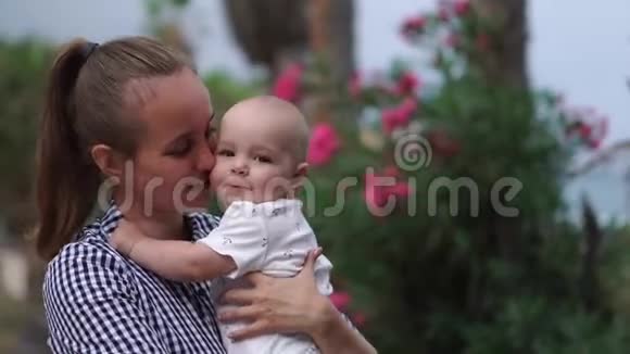 母亲对孩子玩拥抱和亲吻婴儿周围棕榈树与花在度假胜地幸福家庭视频的预览图