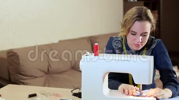 一位年轻的女裁缝在家里的桌子上用一台白色缝纫机工作她创造了新衣服视频的预览图