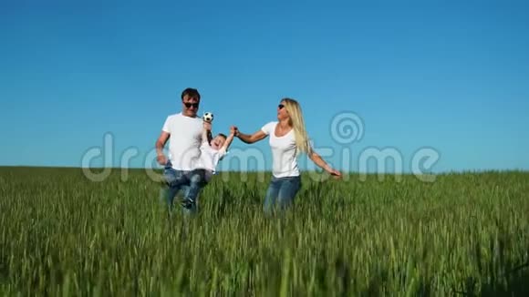 幸福的家庭爸爸妈妈和儿子穿着白色的t恤衫和牛仔裤在田野里跳着笑视频的预览图