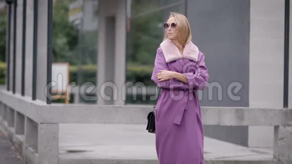 迷人的金发女人穿着时尚的紫色服装在雨天寒冷的秋天等在外面视频的预览图