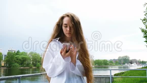 美丽的年轻欧洲女孩在大自然中使用智能手机慢动作长发女人看着电话视频的预览图