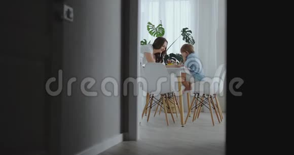 年轻漂亮的妈妈和两个儿子坐在厨房的桌子旁用彩色铅笔画画相机在里面移动视频的预览图