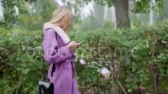 侧面看时尚金发女人走路和盯着智能手机户外视频的预览图