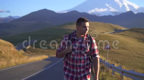 肖像男游客背着背包走在通往山区的道路上视频的预览图