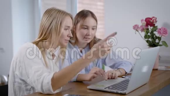 两位年轻女性坐在厨房里在笔记本电脑上上网在互联网上玩得开心的肖像最好的朋友视频的预览图