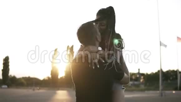 英俊时尚的男孩抱着他苗条的女朋友穿着牛仔衬衫在夏天的黄昏站在路上年轻漂亮视频的预览图