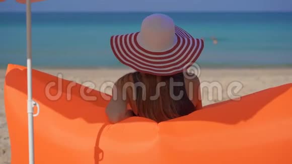 一位年轻女子坐在一张充气沙发上的热带海滩上的慢镜头暑假概念视频的预览图