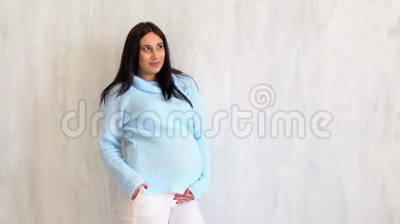 穿着蓝色毛衣的孕妇站在白色的墙上视频的预览图
