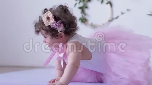 穿着粉色裙子的小女孩在室内的白色背景下爬行视频的预览图