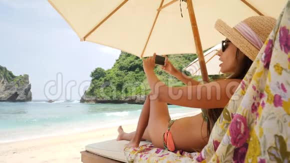 混合种族年轻旅游妇女带着智能手机在热带岛附近的海边休闲床上放松女孩视频的预览图