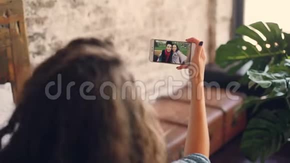 黑发女人用智能手机在线与女性朋友交谈女孩看着屏幕拿着设备和视频的预览图